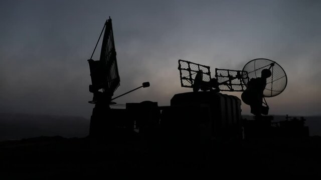 Creative artwork decoration. Silhouette of mobile air defence truck with radar antenna during sunset. Rocket launcher aimed at sky ready to attack. Selective focus