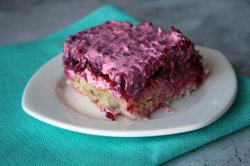 Layered salad of herring, potatoes and beets with mayonnaise in a white plate.