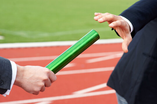 Businessmen pass on the baton in relay race in stadium