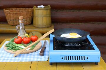 Cooking scrambled eggs with herbs and tomatoes on the gas stove on the terrace. 