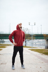 Athletic sporty man training in hoodie sweatshirt in urban city park.