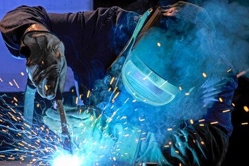 industry - welder in action with face shield, overalls and gloves
