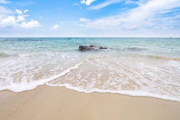 Soft ocean wave on sandy beach with blue sky.