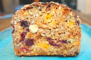 A piece of bread with dried fruits on blue plate, dried apricots, raisins, prunes and hazelnuts, top view.