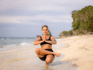One-legged asana. Active woman practicing Padangushthasana, Tiptoe Balance. Yoga on the beach. Balance and concentration. Strong healthy body. Yoga retreat. Copy space. Thomas beach, Bali