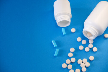 Medicine and healthcare concept. Capsules, tablets scattered near containers on a blue background. Place for your text.
