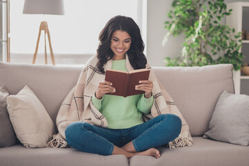 Full size photo of young afro woman happy positive smile sit sofa comfort cozy blanket read book literature novel home