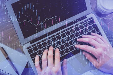 Double exposure of man's hands typing over computer keyboard and forex graph hologram drawing. Top view. Financial markets concept.