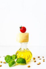 Olivenöl in einer Glasflasche, Parmesan und eine Cocktailtomate gestapelt. Frisches Basilikum und Pinienkerne. Weißer isolierter Hintergrund. Mediterrane Küche.