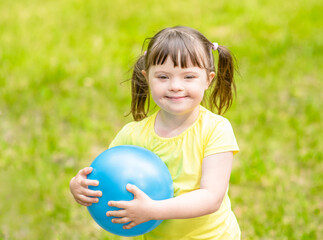 Smiling little girl with syndrome down holds ball in a summer park