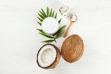 Fototapeta na wymiar Coconut as a food source and cosmetic product. Cracked fruit, a jar of moisturizing cream, wooden spoon and a palm leaf on wood textured table. Close up, top view, copy space, flat lay, background.