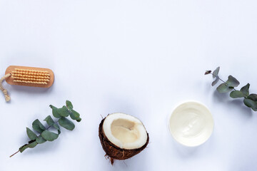 Body brush, natural cream in a jar, coconut and eucalyptus leaves on white background. Personal hygiene and natural cosmetics concept. Top view, flat lay, copy space