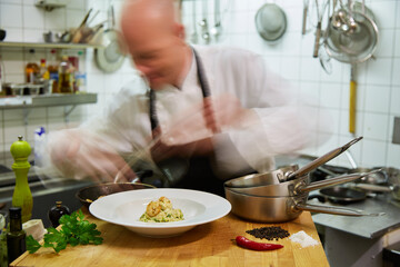 A chef is preparing a dish with seafood. His movements are very fast, so he is blurred. The food is sharply pictured. Normal perspective. 