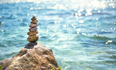 A pyramid of pebbles on a large stone against the background of the sea and the sun's glare on the...