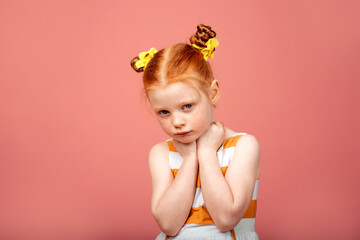 Little girl with red hair on a pink background. Sad and resentful girl.