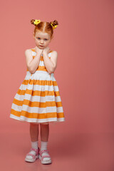 Little girl with red hair on a pink background. Sad and resentful girl.