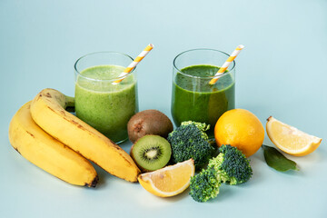 Two green smoothies and ingredients: banana, kiwi, broccoli, lemon on blue background, close up. Healthy raw vegan food concept. Selective focus