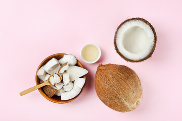 Coconut as a food source and cosmetic product. Cracked fruit in a wooden bowl with a jar of moisturizing oil on pink tabletop. Close up, top view, copy space, flat lay, background.