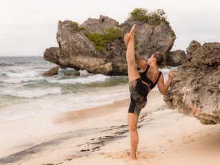 Yoga practice. Caucasian woman practicing Samsahate Hanumanasana, Standing Split Pose. Hamstrings stretching. Balance and concentration. Yoga retreat. View from back. Thomas beach, Bali