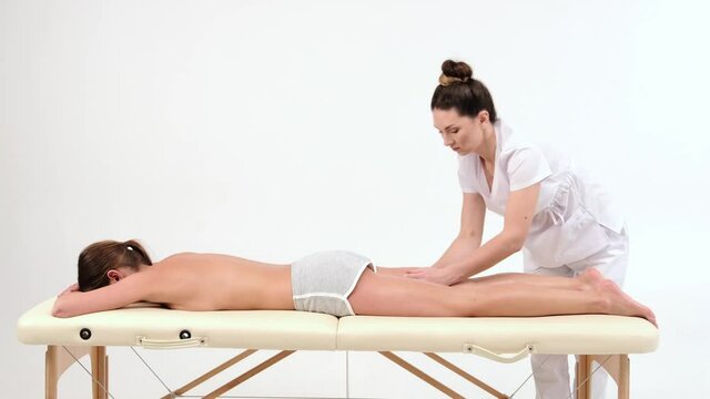 woman lying on a portable massage table on a white background. The therapist's hands are massaging the young woman's legs and foot. Spa, concept massage, aromatherapy