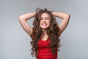 Depressed desperate young brunette woman in red t shirt, holding hands on hair, feeling pain in soul or being angry