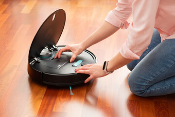 Faceless middle section of young woman emptying the deposit of an automatic vacuum cleaner to clean...