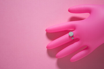 Creative photo with air inflated pink glove and pseudo diamond ring on pink background.