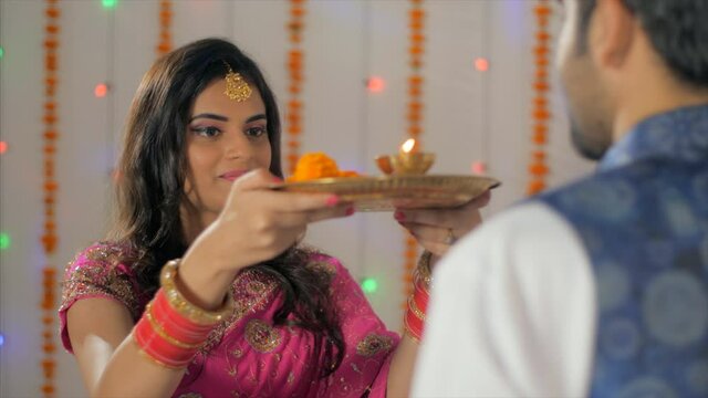 Indian husband-wife happily celebrating the Karwa Chauth festival together. Over the shoulder shot - Newly-wed woman doing Karwa Chauth Puja of her husband against the festival background