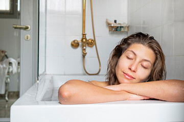 Obraz premium Close up portrait of a beautiful smiling young woman relaxing in a bathtub. Happy brunette female chilling in a bath of hotel room. Copy space, background.