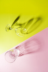 Two empty glass, crystal glasses (top view) lie on a yellow and pink paper background, vertical photo