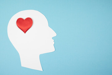 Paper silhouette of a head with a red heart on a blue background. Top view, place for text.