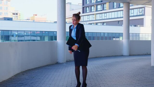 A woman in office clothes is dancing on the background of a modern building. An excited young business woman is celebrating success or the end of the working day