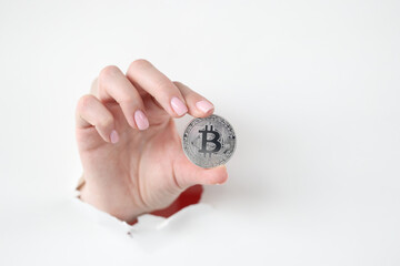 Hand holds silver bitcoin through hole in white paper