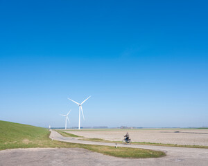 Fototapeta na wymiar man on bicycle and wind turbines in rural landscape of schouwen duiveland in dutch province of zeeland