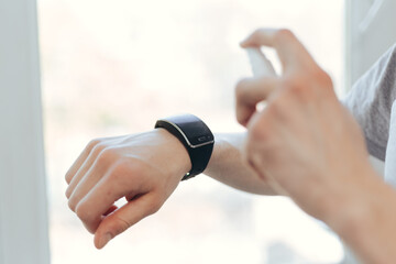 young man is spraying alcohol antiseptic on his smart watch.