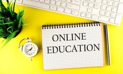 Online Education text on notebook with keyboard , pen and alarm clock on the yellow background
