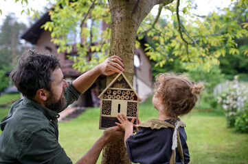 Small girl with father holding bug and insect hotel in garden, sustainable lifestyle.