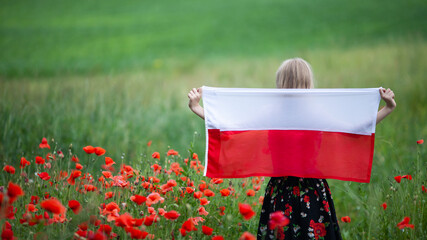 Blond girl holding flag of Poland in the poppy field. Back view. Polish Flag Day. Independence Day. Travel and learn polish language concept.