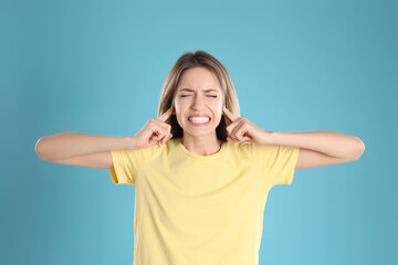 Emotional young woman covering her ears with fingers on light blue background