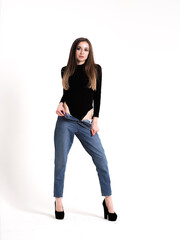 The brunette stands on a white background in a black bodysuit, jeans and high heels