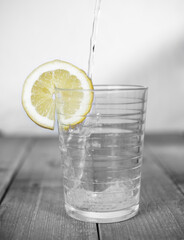 Bicchiere in bianco e nero con limone giallo sole e acqua che viene versata 