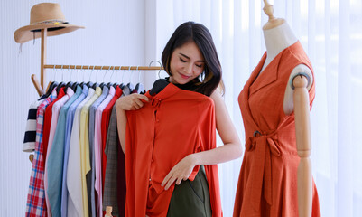 Smiling Asian woman Choose and try on clothe orange color in the Tailor shop. Fashion designer...