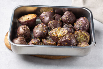 Oven baked  purple potatoes with herbs and salt in metal baking dish on gray background. Home cooking. Vegetarian, plant-based or vegan food concept.