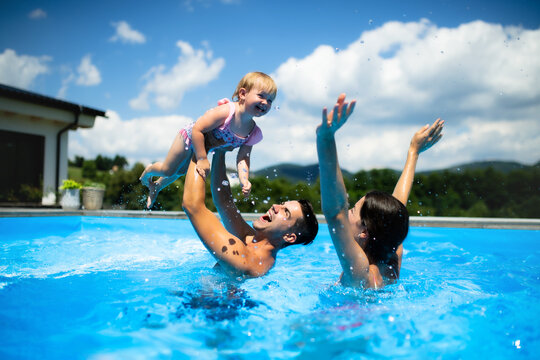 Young family with small daughter in swimming pool outdoors in backyard garden, playing.