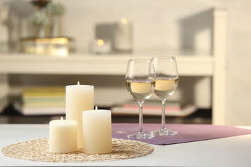 Burning candles and glasses of wine on white table indoors