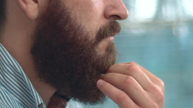 Close up footage of bearded man touching his beard and thinking