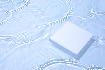 Empty white square podium on transparent clear calm blue water texture with splashes and waves in...