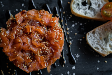 Salmon tartar on blackboard plate with toast and tomatoes