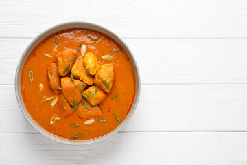 Bowl of delicious chicken curry on white wooden table, top view. Space for text