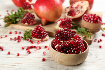 Delicious ripe pomegranate kernels in bowl on white wooden table